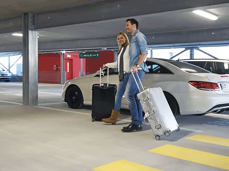 Reisepaar mit Koffern geht durch ein helles Parkhaus am Flughafen Bremen zum Ausgang